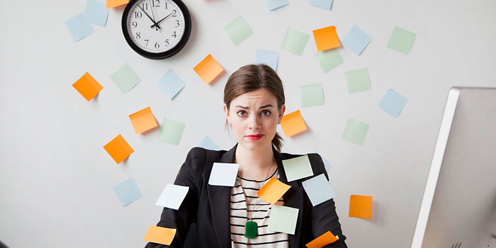 خانمی در دفتر پشت میز نشسته در حال که کاغذهای بورد اسکرام یا کانبان به طور نا مرتب دورش قرار دارند و روی دیوار ساعت نصب شده است