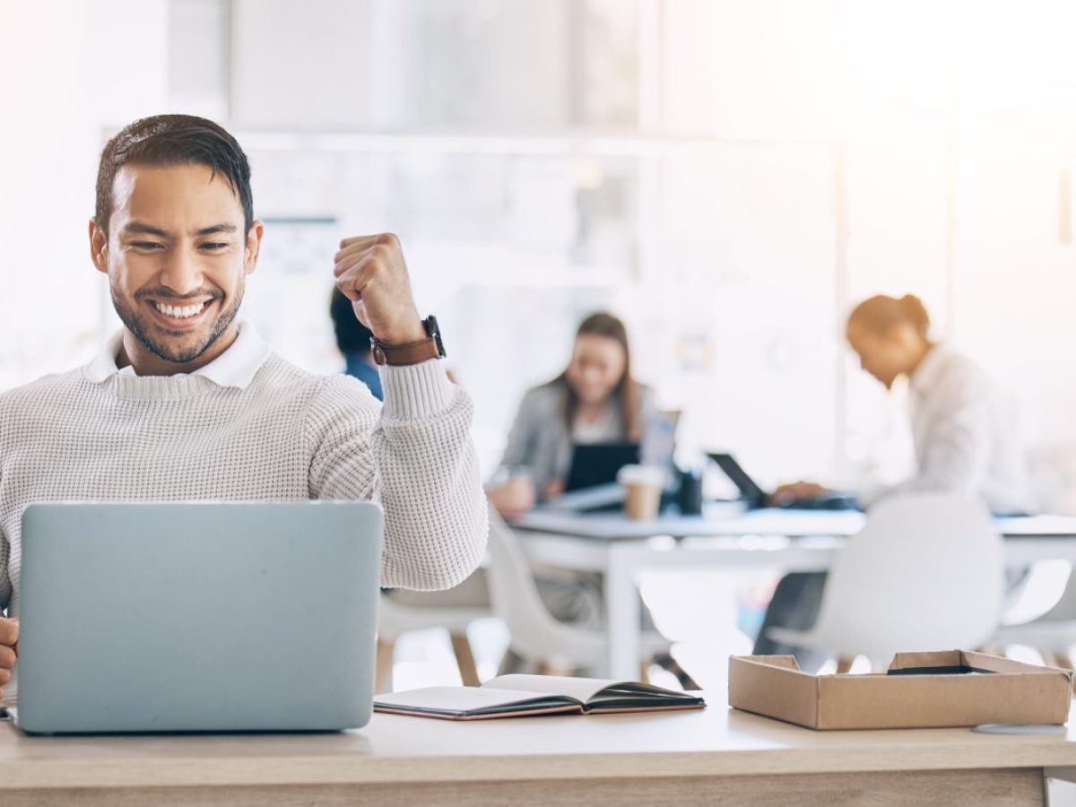 مردی شاد با مشت گره کرده پشت لپ تاپ در محیط دفتر